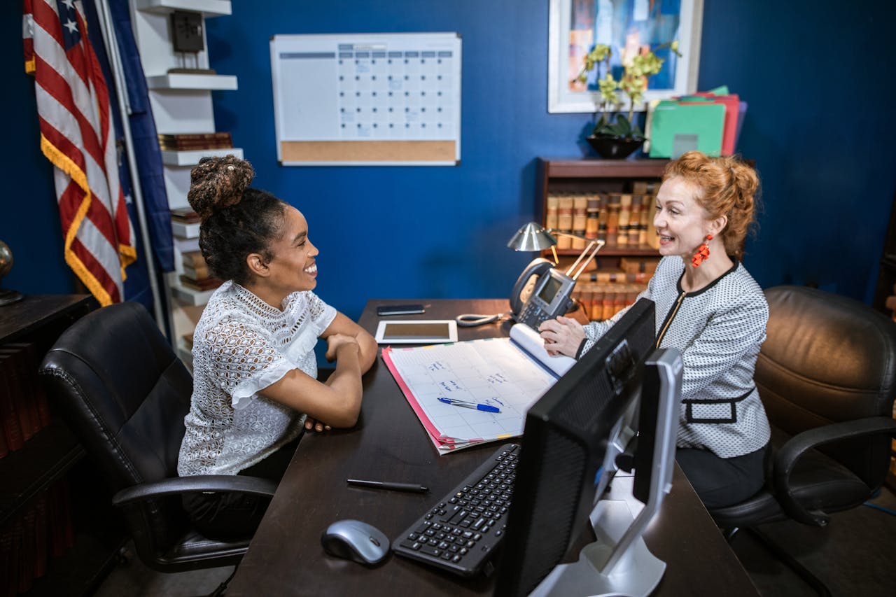 About Two professional women discussing at an office desk, showcasing leadership and collaboration.