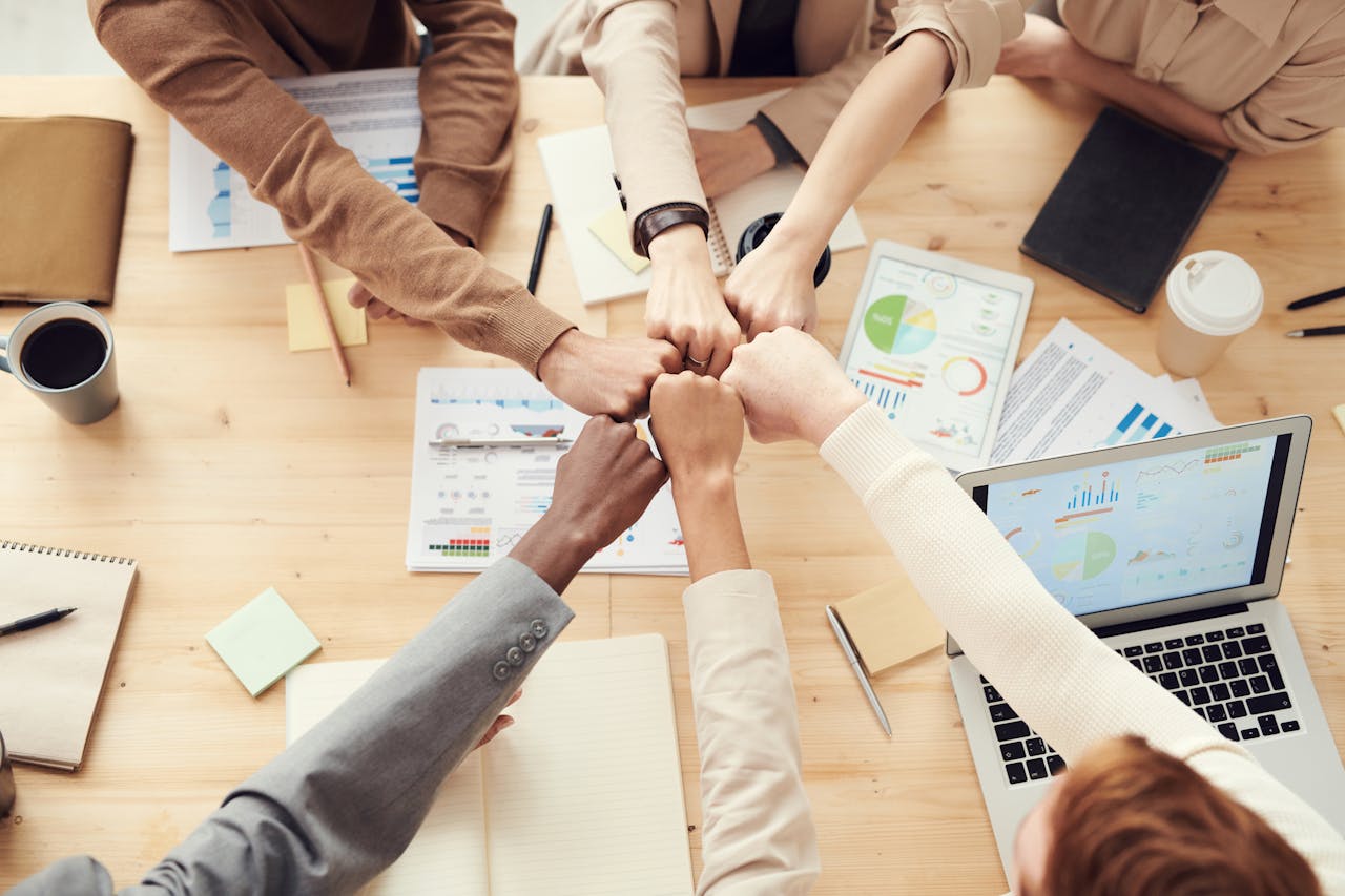 Home Top view of a diverse team fist bumping over a meeting table with paperwork and laptops, symbolizing teamwork.